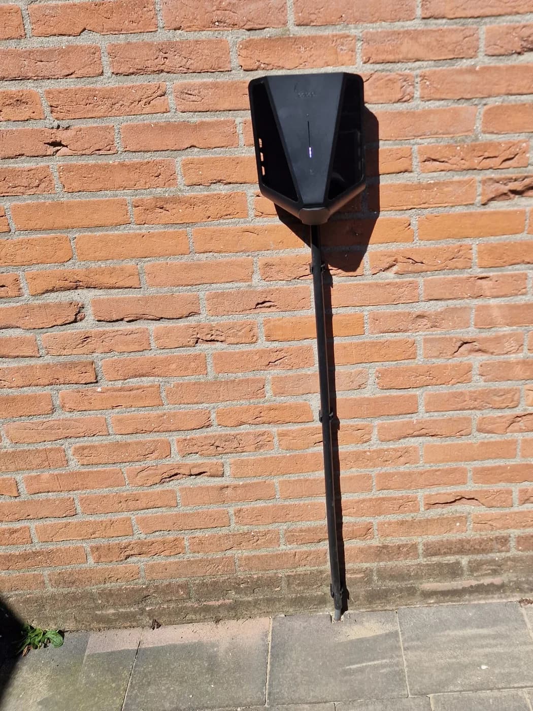 Easee laadpaal op montagepaal bij een bakstenen muur