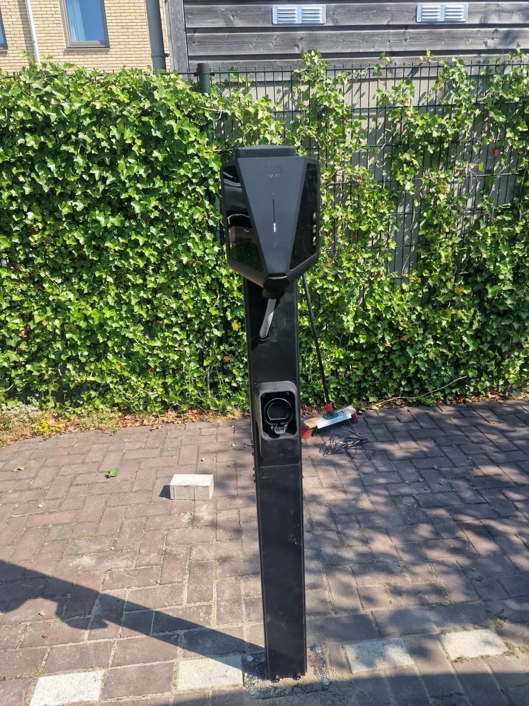 Laadpaal op montagepaal naast een haag