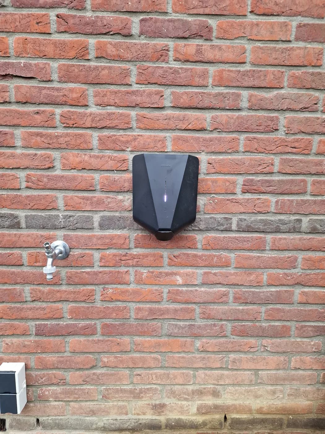 Easee laadpaal aan de gevel naast een buitenkraan